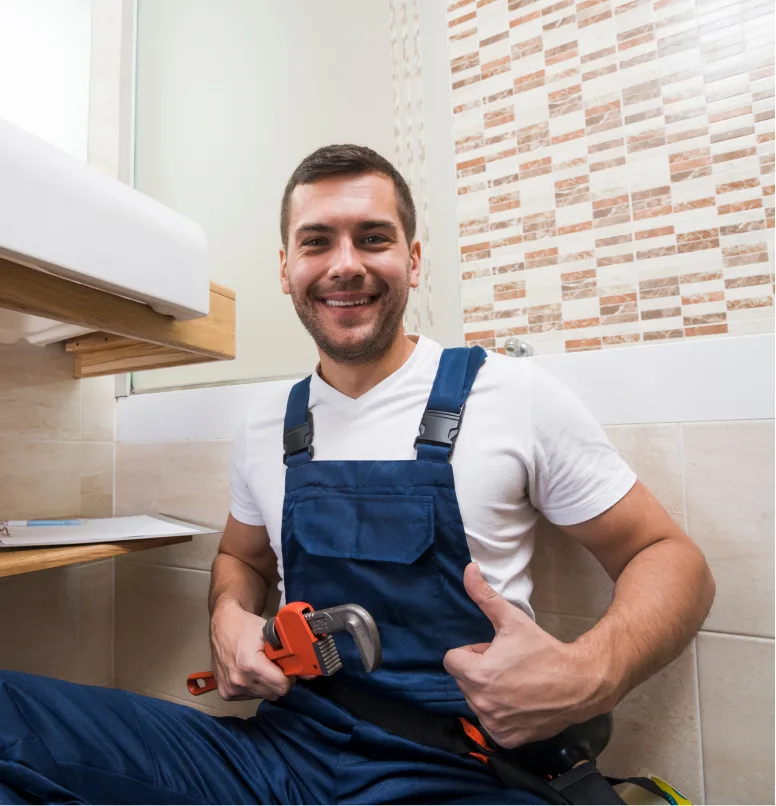 Smiling plumber holding wrench in bathroom.